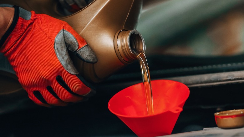 a person pouring fresh oil into their engine using a red funnel