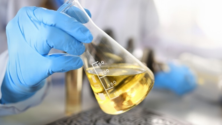 a scientist holding a flask of motor oil in a lab