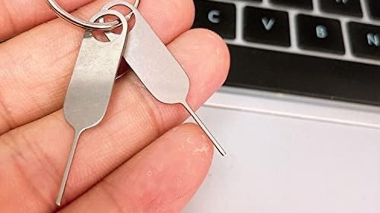 Hands holding two Eaglewireless SIM Card Eject Pins over a laptop.