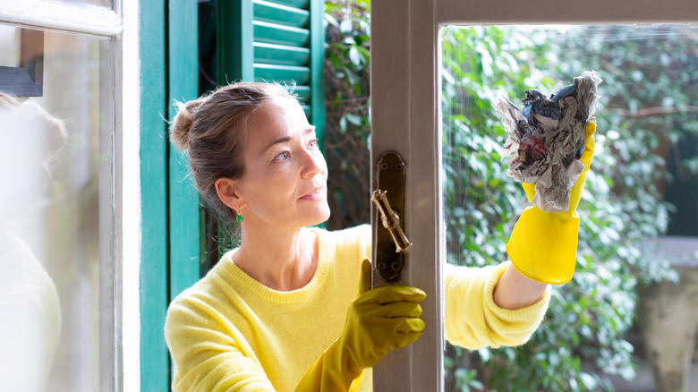 Woman in yellow shirt and gloves cleaning a window