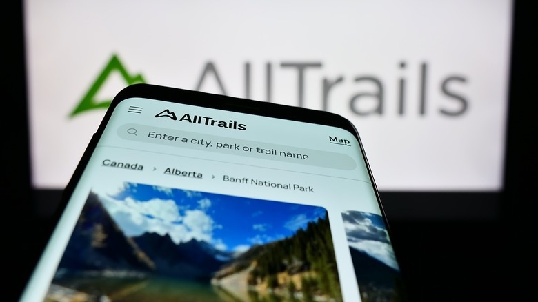 The AllTrails site on a smartphone in front of the AllTrails company logo