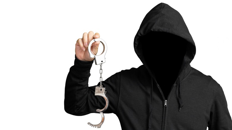 A hooded man holding handcuffs