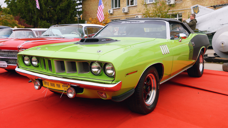 A green Plymouth Hemi Cuda Convertible is parked on a red surface.