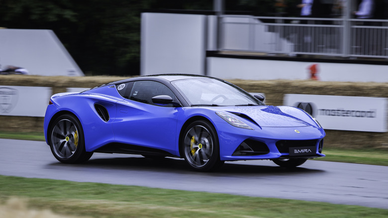 A blue Lotus Emira going up the Goodwood Hillclimb, front 3/4 view