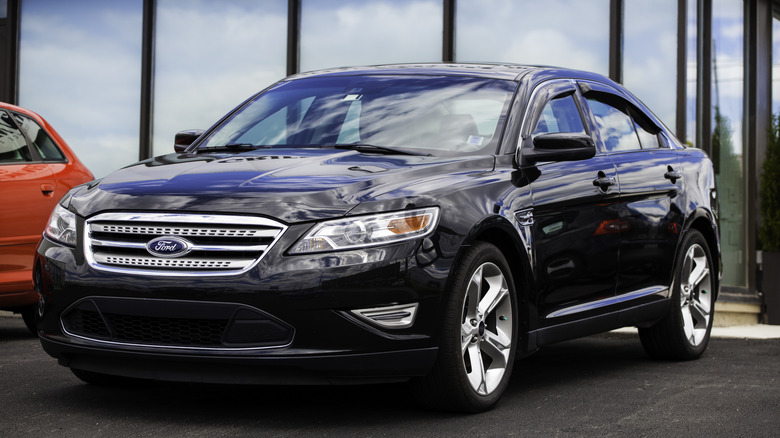 A black pre-facelift Ford Taurus SHO outside a dealership, front 3/4 view