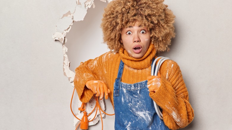 Woman holding extension cord next to broken wall