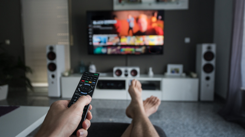 A man with a home theater setup browsing channels with his remote.