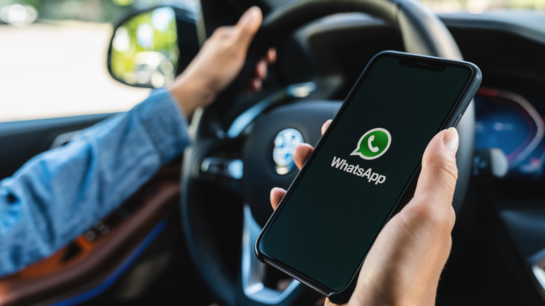 Man holding smartphone with Whatsapp logo in car