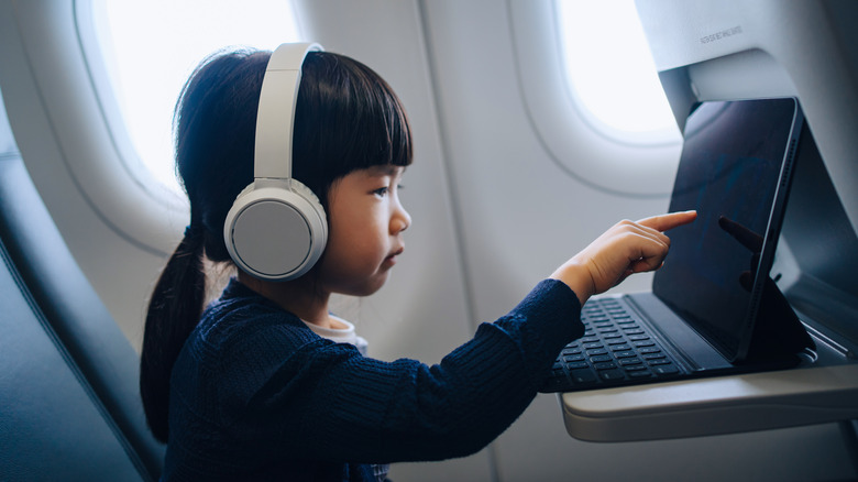 A little girl wearing wireless headphones and touching the touchscreen of a 2-in-1 laptop.