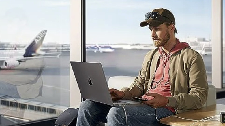 A man charging a MacBook at an airport with an Anker Prime Power Bank. 