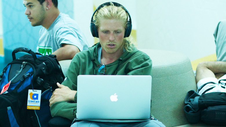 A man using a MacBook on his lap in an airport.