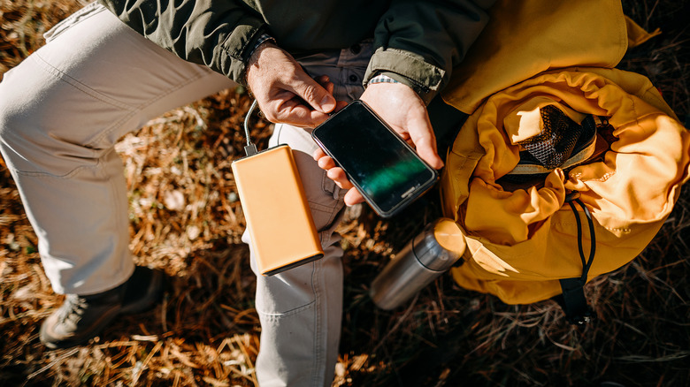 A hiker charging his smartphone with a portable charger.