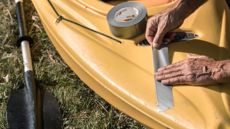 Person applying duct tape to the outside of a yellow kayak.