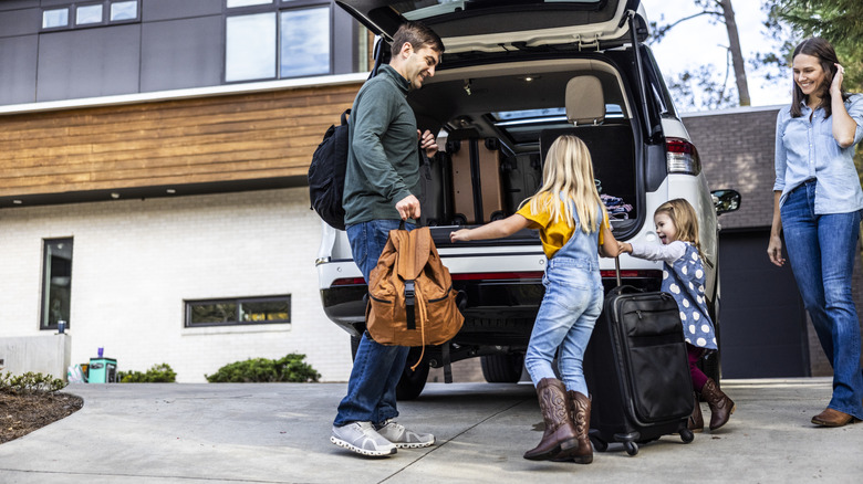 Family of four putting baggage in an open vehicle in a home's driveway