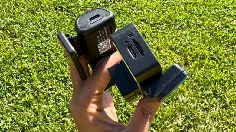 Person holding black electronic components against a grassy background