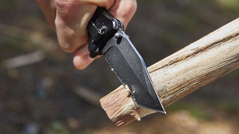 Close-up of an open black pocket knife whittling a stick