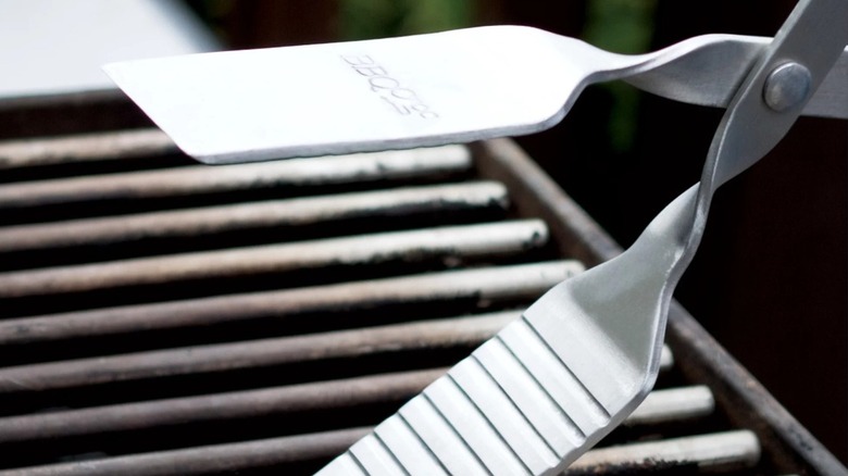 Metal tongs  with a grooved edge aligned with a grill grate