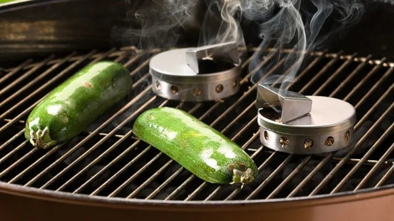 Sliced jalapeno peppers beside two silver disks emitting smoke on a grill