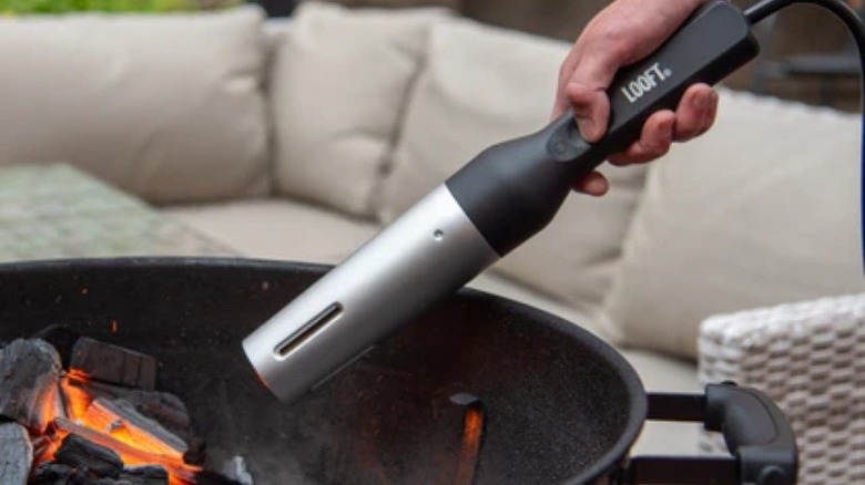 Handheld tool pointed toward charcoal-filled grill