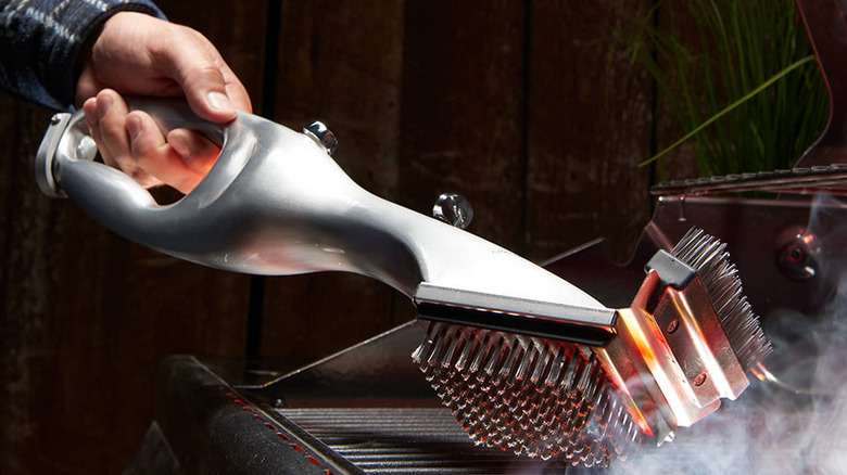 Gray tool with handle emitting steam onto a grill surface