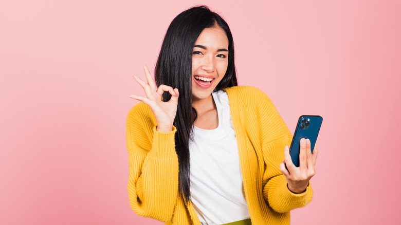 woman gesturing the OK sign and holding a smartphone in the other hand