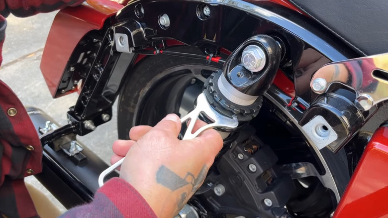 A close view of a motorcycle rear suspension with a man adjusting it with a spanner