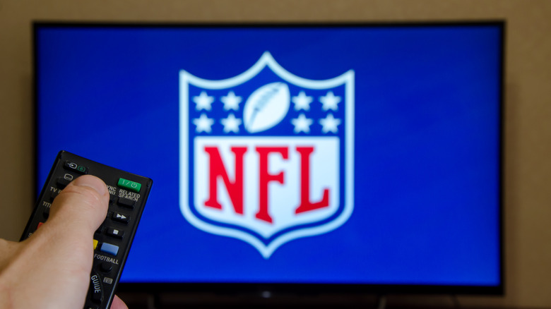 A TV with NFL running on it and a person controllit with a remotre controller