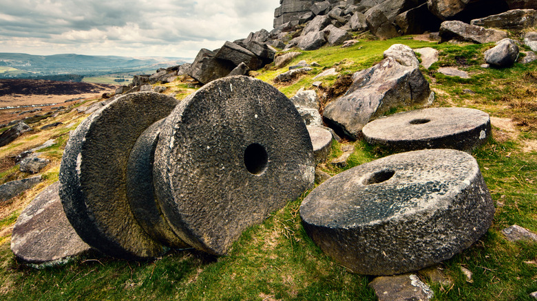 Millstone wheels on a grassy and rocky hillside.