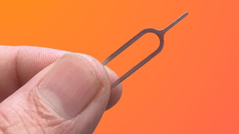 A hand holding out a SIM card eject pin on an orange background.