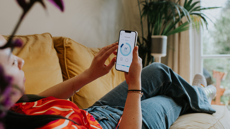 Women lying on couch looking at thermostat settings on smartphone