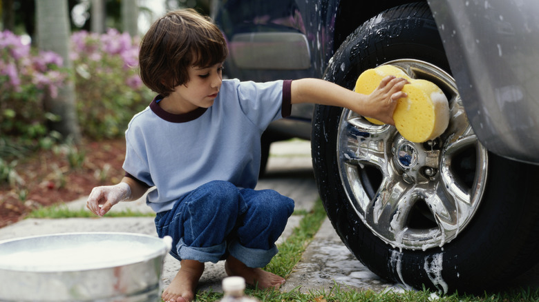 A kid washing the wheel hubs on a car