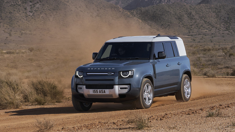 A Land Rover Defender 110 in blue on a dirt trail, front 3/4 view