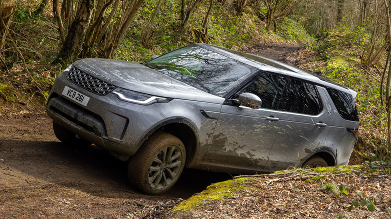 The Land Rover Discovery driving up a muddy hill, front 3/4 view