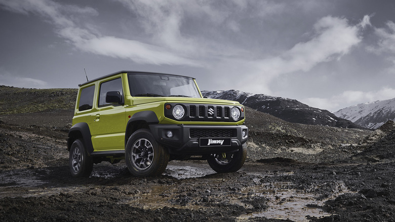 The Suzuki Jimny in lime green on a muddy trail, front 3/4 view