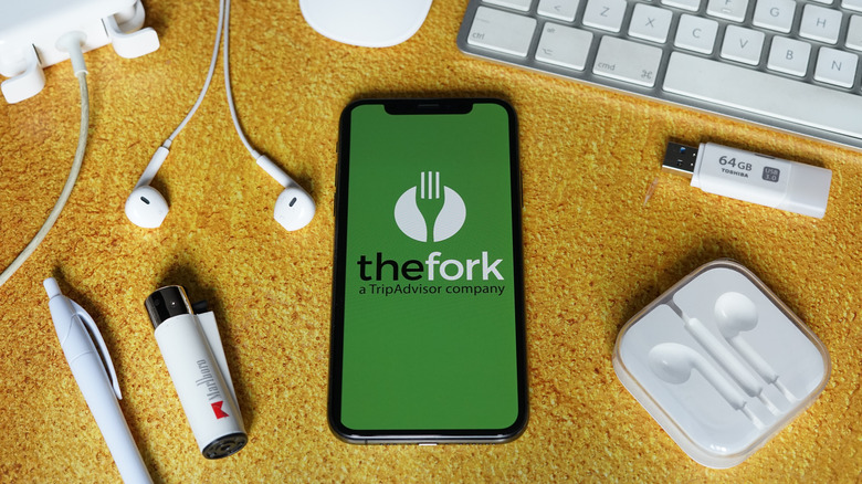 TheFork logo on a smartphone on a desk next to various accessories.