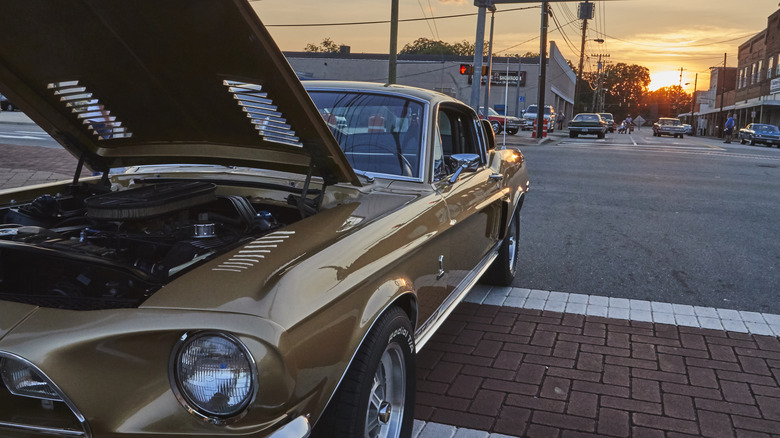 Gold Mustang parked on street at sunset