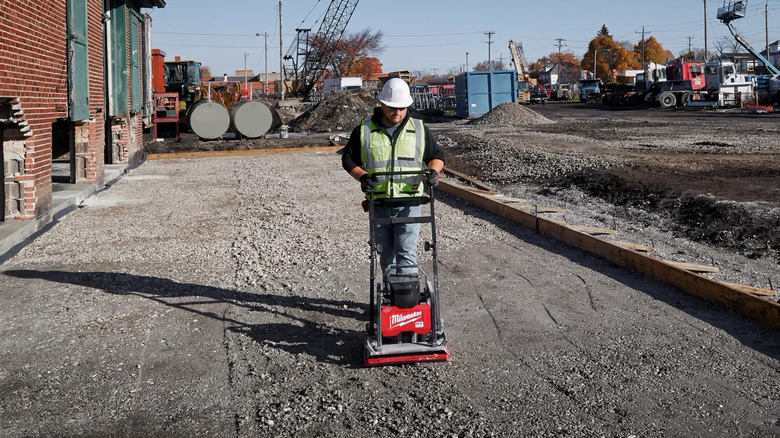 Worker using Milwaukee plate compactor on ground