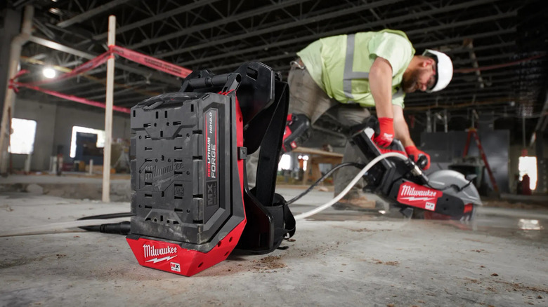 Worker using concrete saw with battery extension pack in foreground