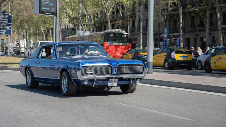 A blue Mercury Cougar driving down the road, front 3/4 view