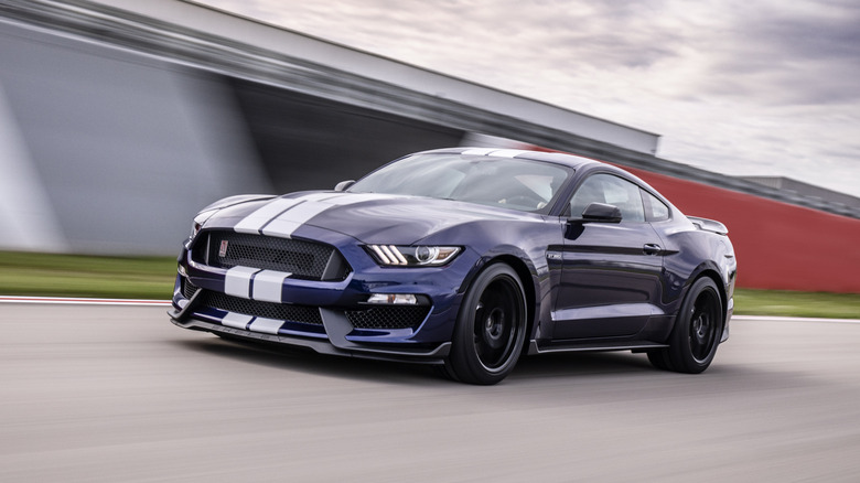 The Shelby GT350 on the racetrack, dark blue with white stripes, front 3/4 view