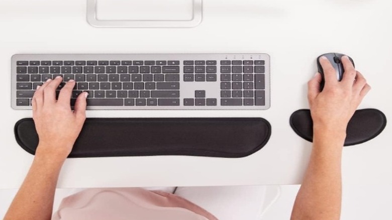 Person using a black keyboard and mouse wrist rest with a computer