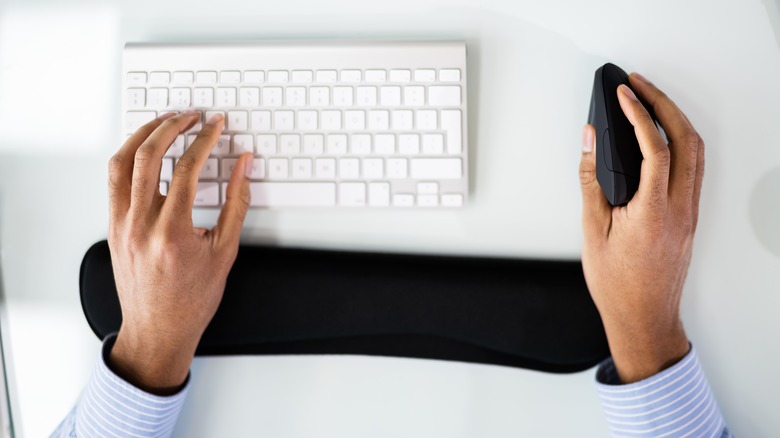 Person's hands resting on a keyboard wrist rest and using an ergonomic mouse