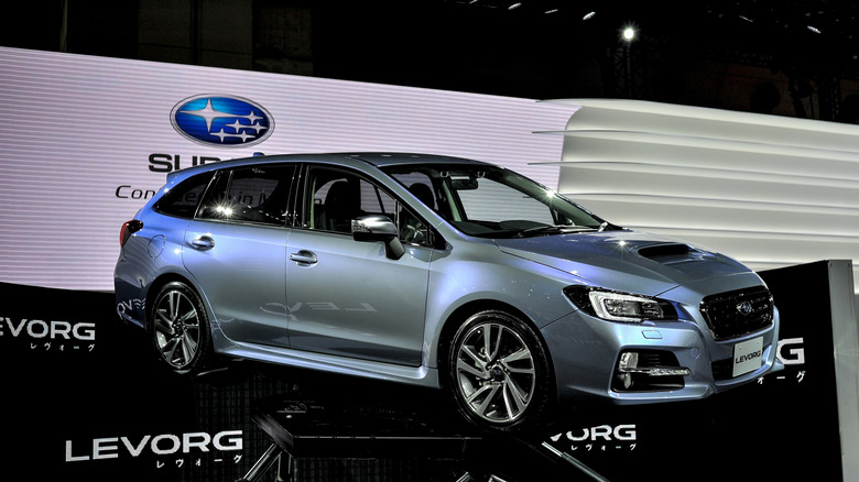 A bluish silver Subaru Levorg suspended in mid-air at an auto show, front 3/4 view