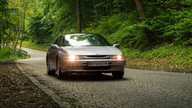 A Subaru SVX driving on a mountain road, front view, silver exterior