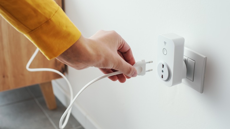 Unseen person plugging a cord into a smart plug which is plugged into a wall outlet