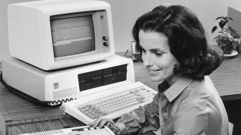 A woman working on an IBM 5150 PC in black and white