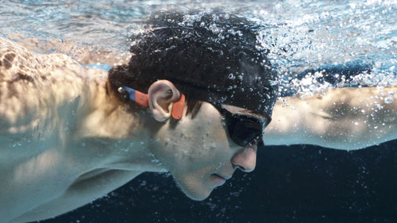 A man swimming with the SHOKZ OpenSwim Pro headset underwater.