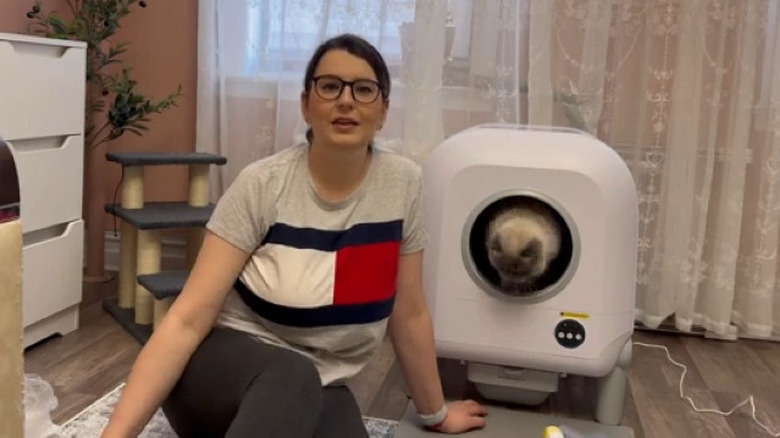 Person sitting next to smart litter box with cat inside