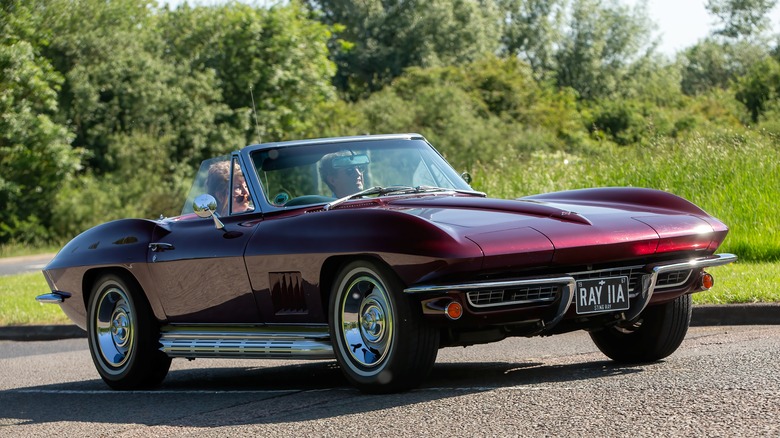 A maroon Corvette cruising on a country road