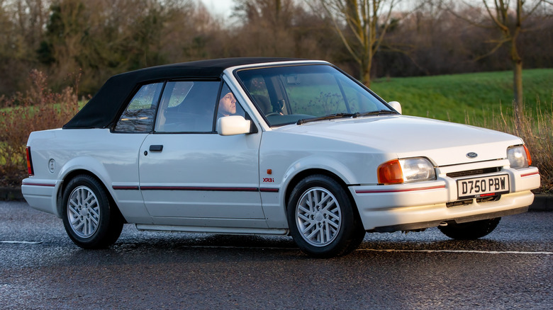 A white Ford Escort XR3i driving on an English country road